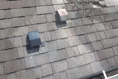 Shingle roof with two vents and damage.